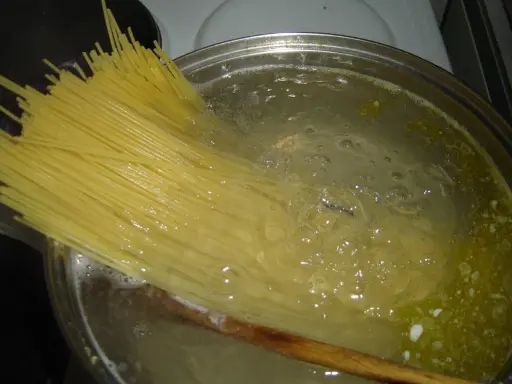 Długi makaron spaghetti zanurza się w gotującej wodzie. Czas, ile gotuje się makaron, zależy od jego grubości.