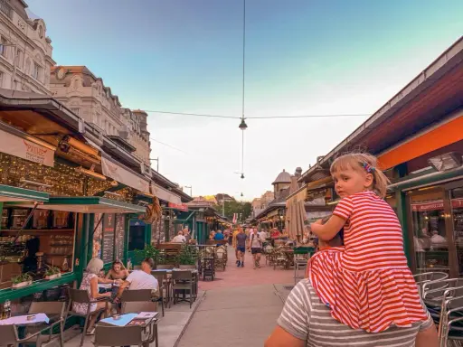 Wiedeń rynek tętni życiem. Dziewczynka na ramionach taty podziwia gwarne uliczki z restauracjami i sklepikami.