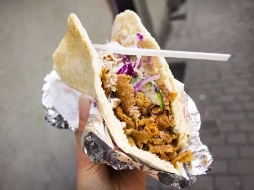 Pyszny kebab w bułce z mięsem, warzywami i sosem. To danie, które swoją popularność zawdzięcza podróżom i wymianie kulturowej, pokazując skąd pochodzi kebab.