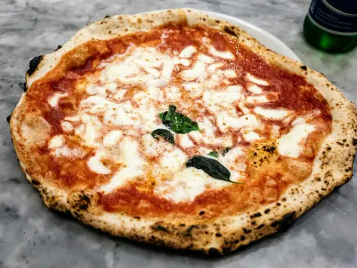 Pyszna pizza napoletana z rozpływającym się serem mozzarella i aromatycznym sosem pomidorowym, ozdobiona świeżą bazylią.