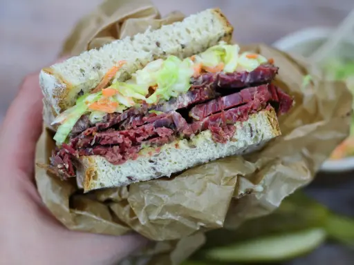Pyszna kanapka z pastrami, z chrupiącą surówką i musztardą, zawinięta w papier.