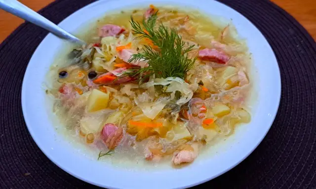 Syta zupa z kiszonej kapusty z ziemniakami i kiełbasą, ozdobiona koperkiem. Pyszne dania z kapusty na zimowe wieczory.