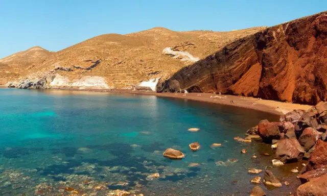 Santorini plaże: Czerwona plaża z turkusową wodą i skalistymi klifami.