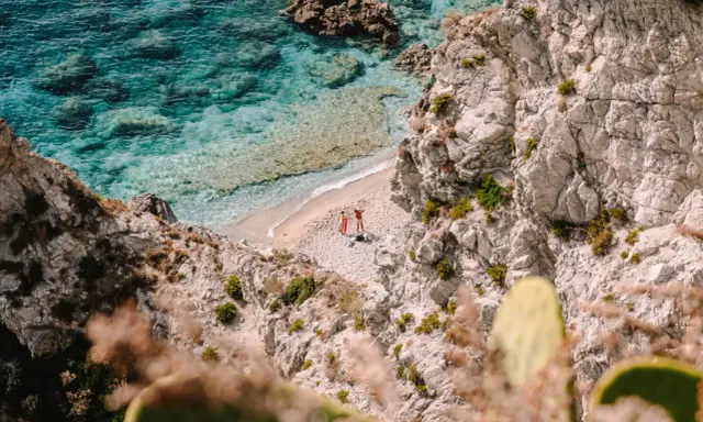 Malownicza zatoczka na Kalabrii, gdzie warto zobaczyć turkusowe morze i skaliste wybrzeże. Dwie osoby odpoczywają na piaszczystej plaży.