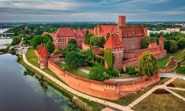 Potężny zamek w Malborku, największy zamek na świecie, otoczony murami obronnymi i rzeką, z czerwonymi dachami i wieżami.
