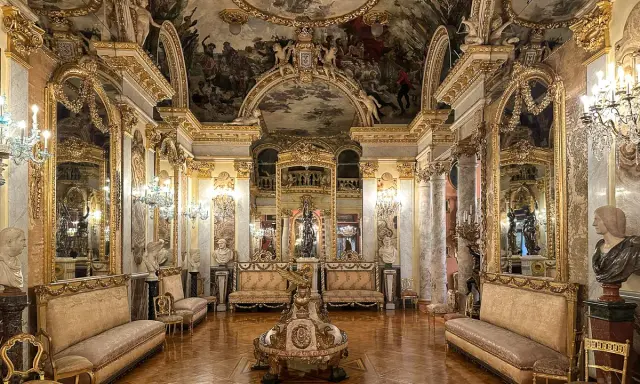 Złocone wnętrze muzeum w Madrycie, z malowanym sufitem, lustrami i antycznymi meblami.