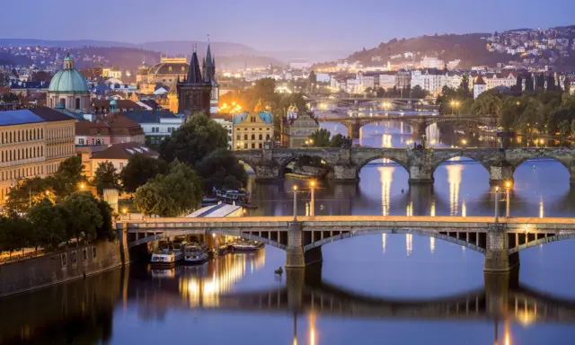 Praga nocą, z licznymi mostami na Wełtawie i oświetlonymi budynkami. Ciekawe ciekawostki o Czechach czekają na odkrycie w tym magicznym mieście.