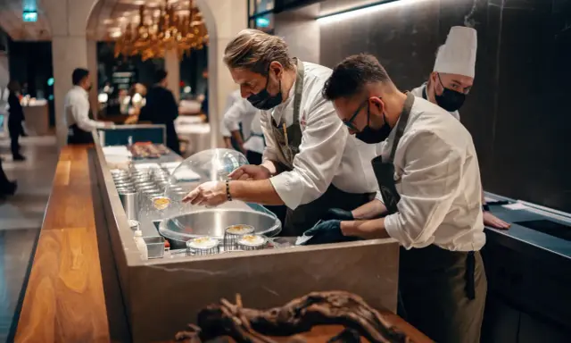 Szefowie kuchni w atelier amaro przygotowują dania. W tle widać eleganckie wnętrze restauracji.