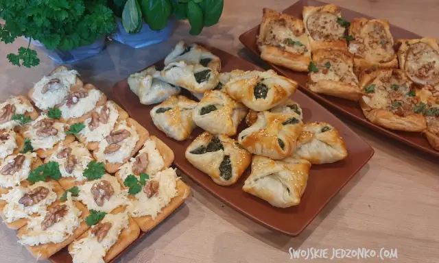 Na stole trzy rodzaje przekąsek: krakersy z pastą serową i orzechami, pieczone ciastka z nadzieniem szpinakowym i kwadratowe tartaletki z farszem. Idealna szybka przekąska na imprezę.