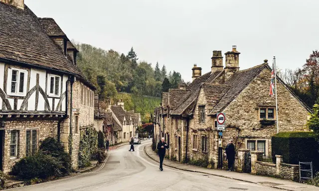 Kamienna uliczka w Cotswolds, z tradycyjnymi domami i drzewami na wzgórzach.