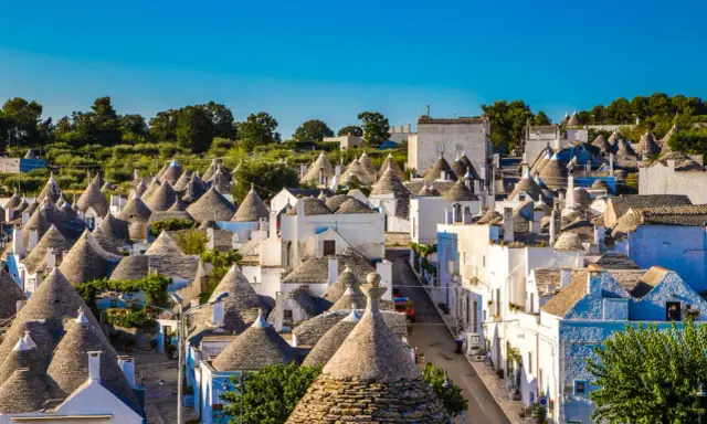 Urokliwe trulli w Alberobello, z ich stożkowymi dachami, tworzą bajkowy krajobraz pod błękitnym niebem.