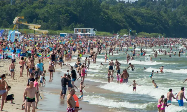 Tłumy ludzi na plaży i w wodzie, zjeżdżalnie wodne w tle. Idealne miejsce na wakacje w Polsce!