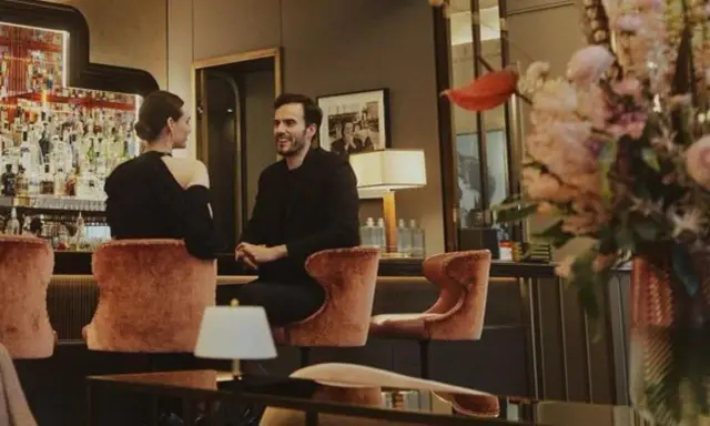 Para w eleganckim barze w Warszawie, uśmiechnięci, siedzą na aksamitnych stołkach. Idealna randka w stolicy.