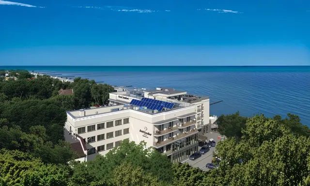 Nowoczesny hotel z panelami słonecznymi nad polskim morzem, otoczony zielenią.