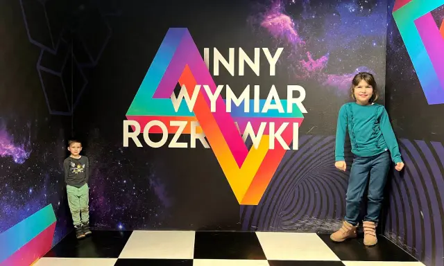 Dzieci w "Innym Wymiarze Rozrywki" w Warszawie. Kolorowa ściana z motywem kosmosu i geometrycznymi kształtami.