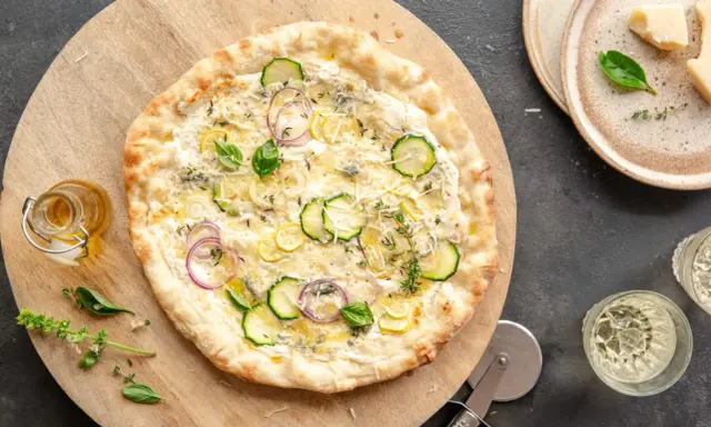 Pyszna pizza bianca z cukinią, cebulą i cytryną, podana na drewnianej desce.