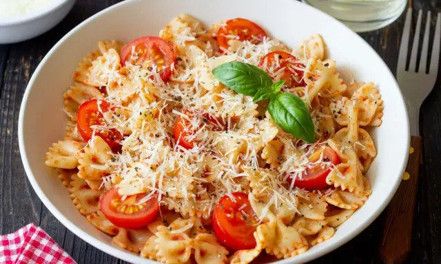 Pyszny makaron farfalle z pomidorkami koktajlowymi i parmezanem, idealny na kolację.