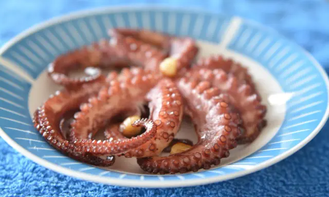 Gotowy ośmiornica przepis na talerzu z niebieskimi paskami. Delikatne macki z czosnkiem, idealne do degustacji.
