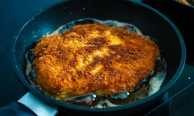 Złocisty kotlet schabowy smaży się na patelni. Idealnie chrupiąca panierka i bulgoczący tłuszcz świadczą o tym, jak długo smażyć schabowe, by były perfekcyjne.