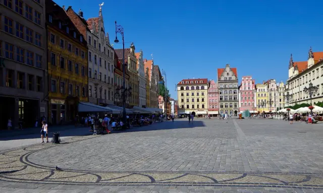 Kolorowy Rynek we Wrocławiu, idealne miejsce na jednodniowe wycieczki z Wrocławia. Ludzie spacerują, siedzą w kawiarniach, ciesząc się słońcem.