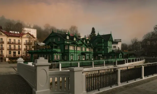 Krynica-Zdrój atrakcje wieczorem: malownicza, zielona willa z restauracją i hotel Mewą w mglistym, jesiennym krajobrazie.