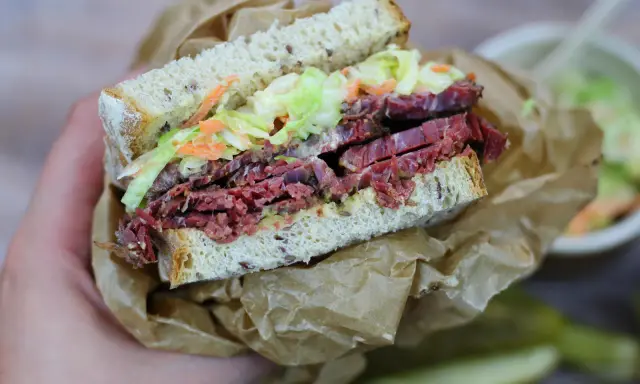 Pyszna kanapka z pastrami, z chrupiącą surówką i musztardą, zawinięta w papier.