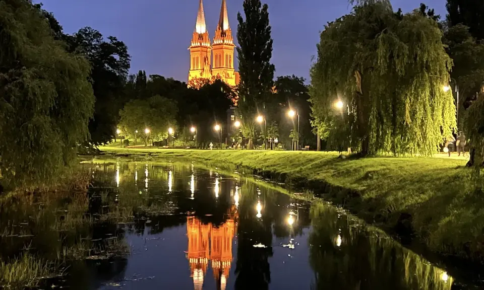 Wieczorny spacer nad rzeką we Włocławku. Podświetlona katedra odbija się w wodzie, tworząc magiczny widok. Idealne włocławek atrakcje na weekend.