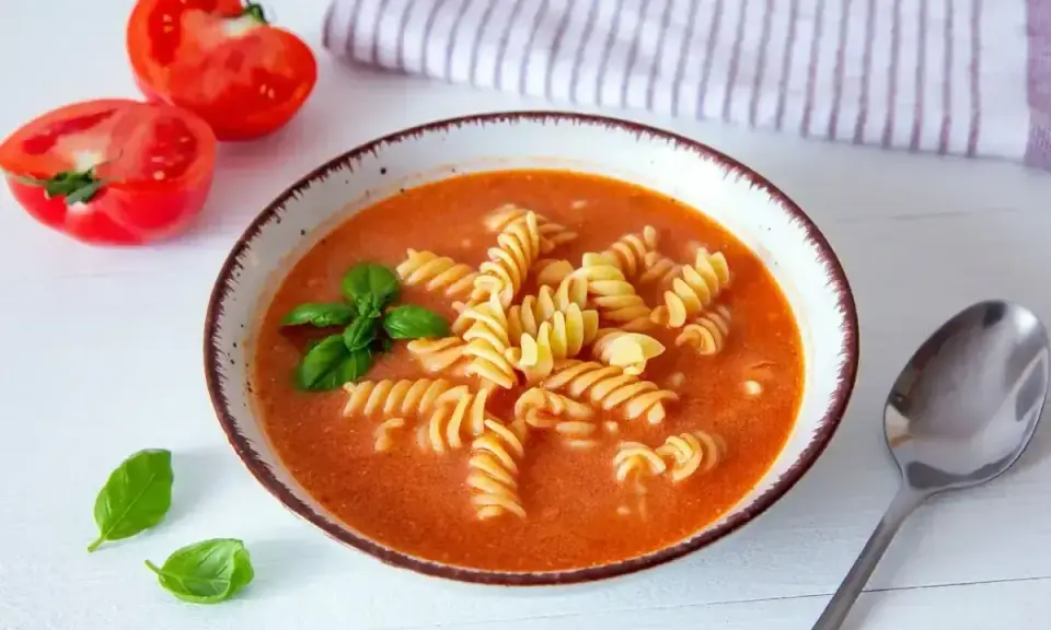 A miseczce zupy pomidorowej z makaronem fusilli, listkami bazylii i połówkami pomidorów obok. Idealne przyprawy do zupy pomidorowej.