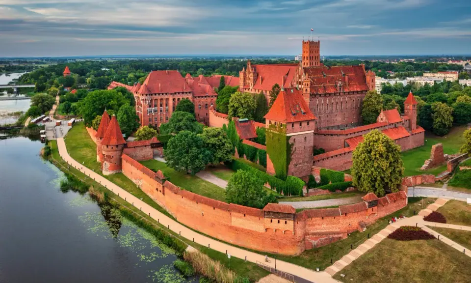 Potężny zamek w Malborku, otoczony murami, z wieżami i zielenią. Ciekawostki o tym miejscu przyciągają turystów.