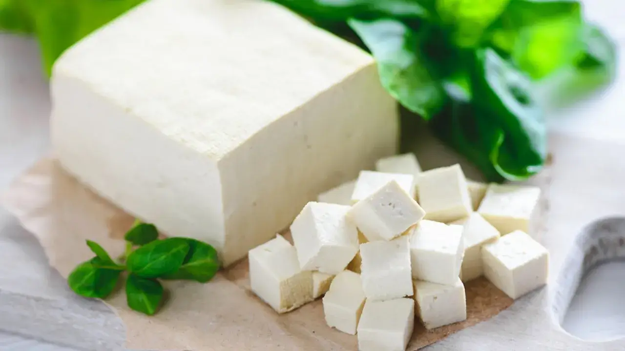 Kostka tofu i pokrojone w kostkę tofu na desce, ozdobione zielonymi liśćmi.