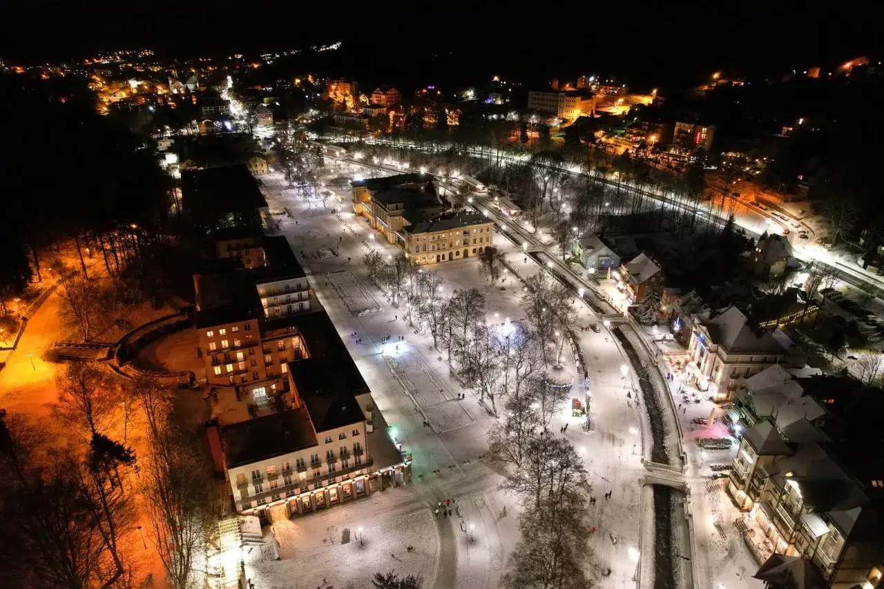 Zimowy wieczór w Krynicy-Zdroju. Oświetlone budynki i deptak tworzą magiczną atmosferę, a śnieg dodaje uroku. Krynica-Zdrój atrakcje wieczorem w całej okazałości.