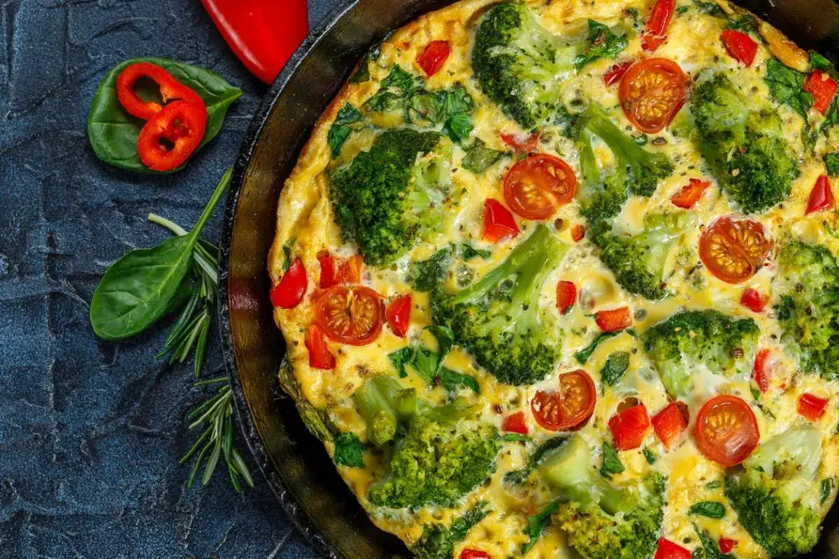 Pyszny omlet wytrawny z brokułami, pomidorkami i papryką, podany na patelni. Idealny na zdrowe śniadanie lub lekki obiad.