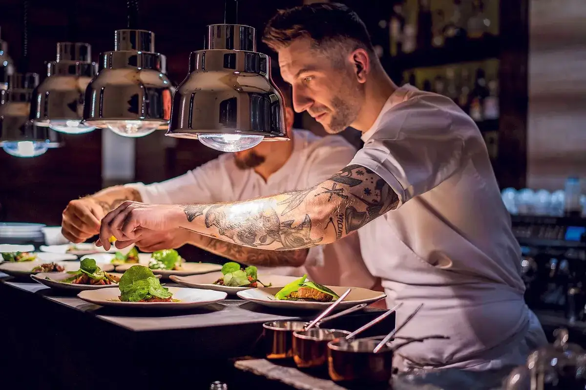 Szef kuchni z tatuażami dopracowuje dania w restauracji z gwiazdką michelin.