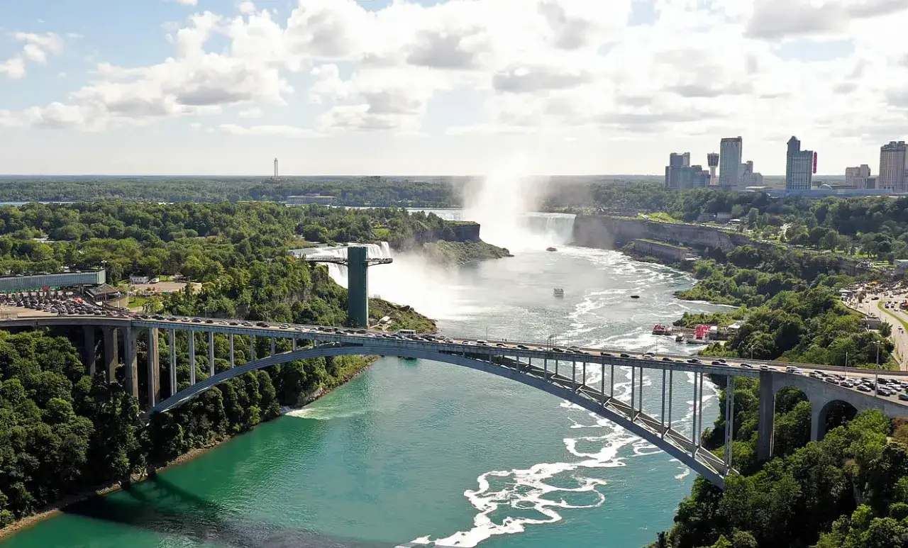 Widok na wodospad Niagara z mostu. W tle widać mgłę unoszącą się nad wodą i budynki. Informacje o wodospadzie Niagara.
