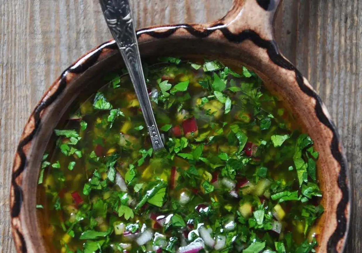 Aromaticzny sos chimichurri w glinianej misce, pełen świeżej pietruszki, czosnku i papryczki chili. Idealny do grillowanych mięs.