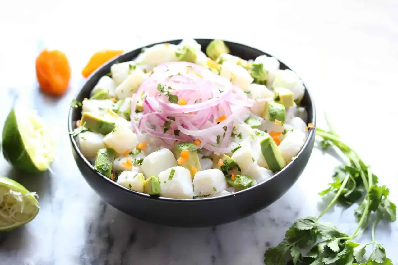 Pyszne ceviche z kawałkami ryby, awokado, czerwoną cebulą i kolendrą, podane z limonką.