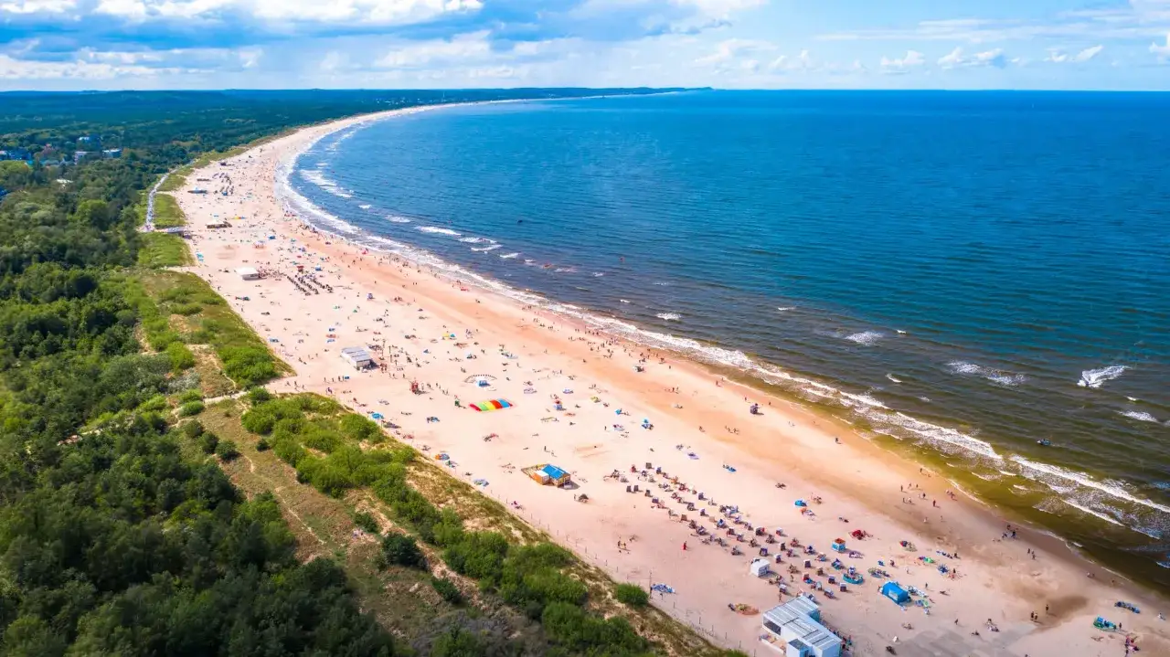 Szeroka, piaszczysta plaża nad Bałtykiem, pełna ludzi wypoczywających na słońcu. Idealne miejsce na wakacje w Polsce.