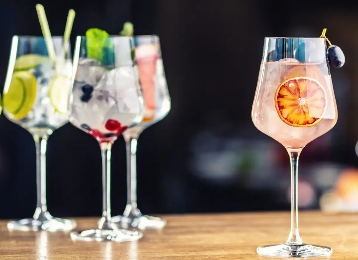 Orzeźwiający drink z ginem, udekorowany plasterkiem pomarańczy i winogronem. W tle inne drinki z owocami.