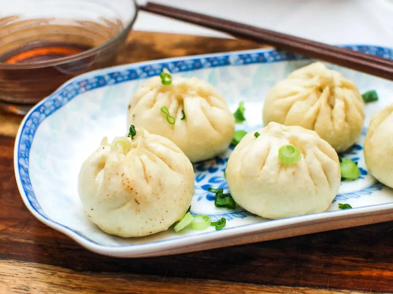 Piękne, parowane pierożki gyoza z zieloną cebulką na talerzu, gotowe do zanurzenia w sosie.