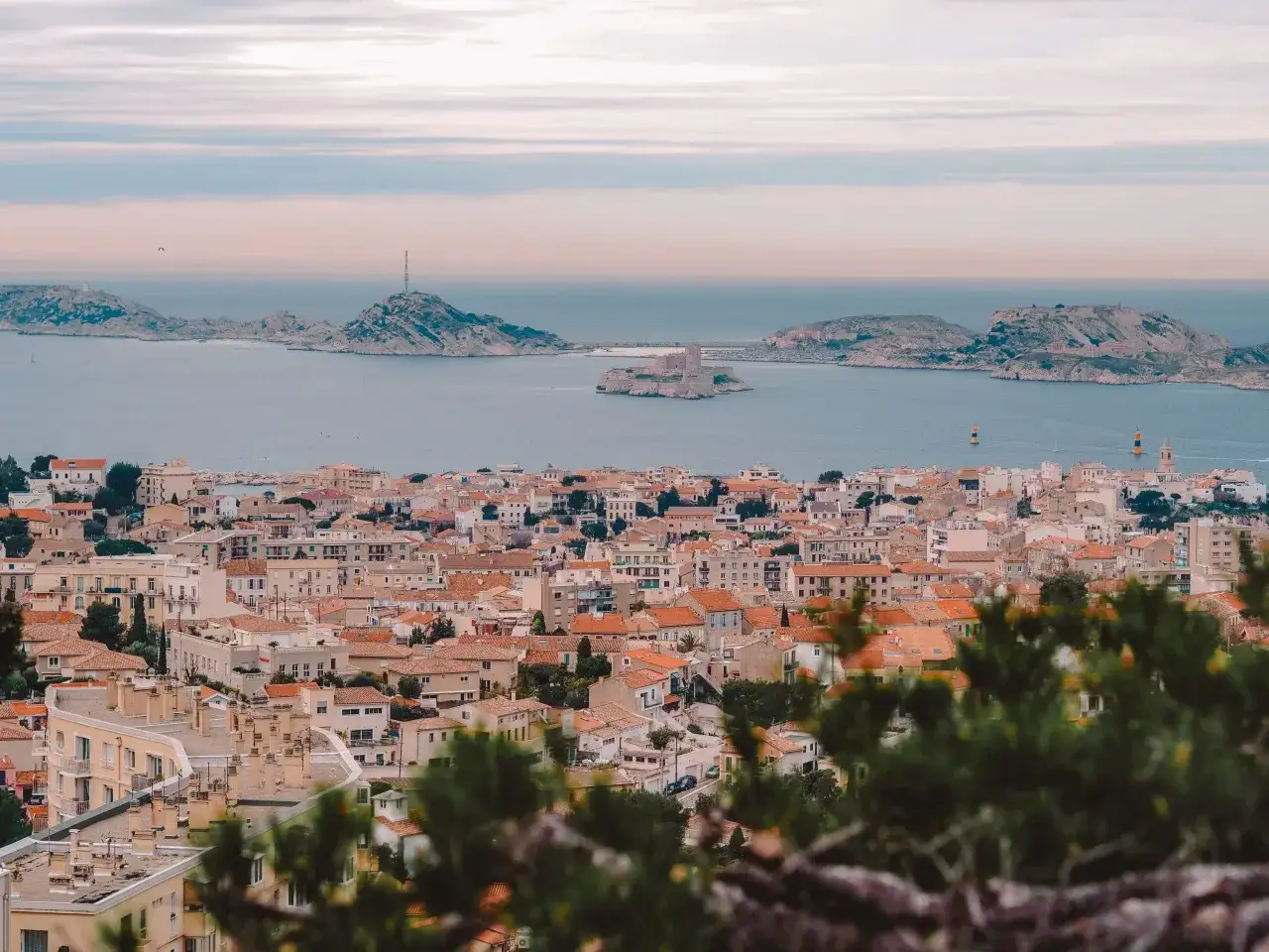 Widok na miasto z dachami i morzem w tle, z widocznym zamkiem na wyspie. To piękne Marseille.