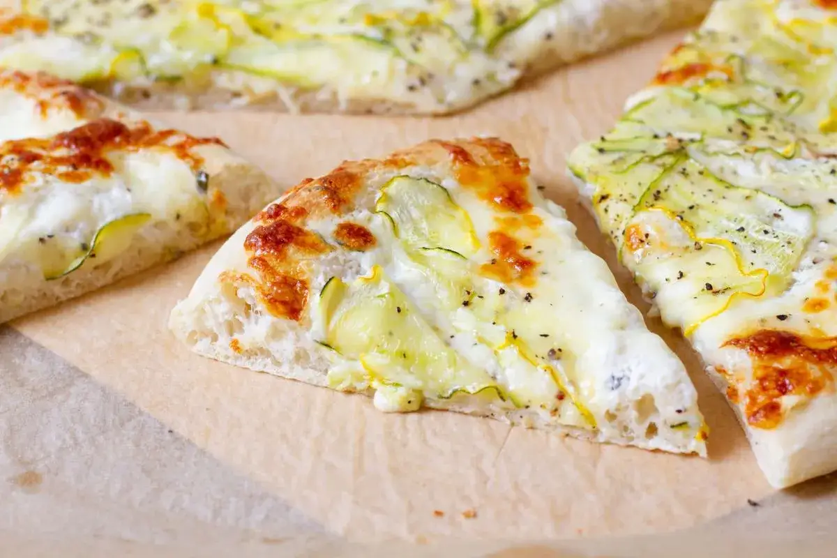 Kawałki pysznej pizzy bianca z cukinią i serem, posypane pieprzem. Idealna na lekki posiłek.