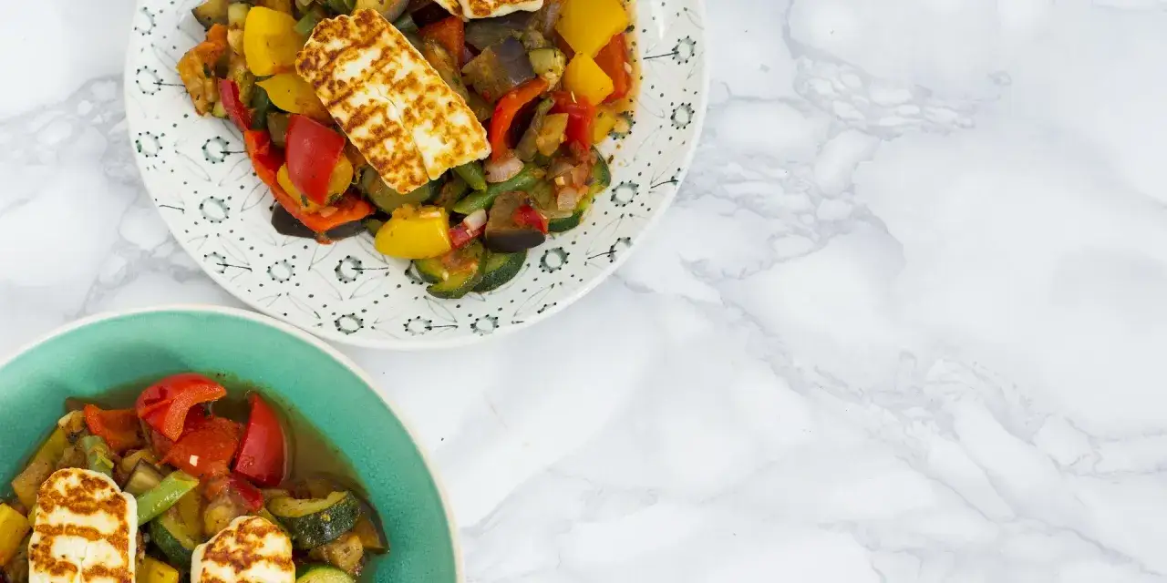 Dwa talerze z grillowanymi warzywami i serem halloumi. Danie wygląda apetycznie i kolorowo.