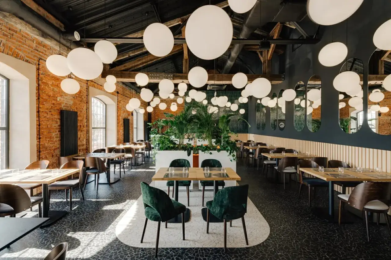 Wnętrze restauracji w Warszawie z ceglanymi ścianami, mnóstwem białych lamp i bujną zielenią. Idealne miejsce na nietypowe restauracje Warszawa.