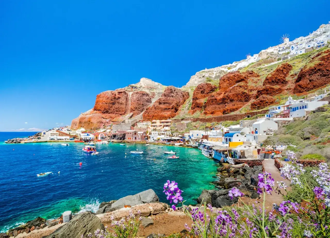 Malownicze Santorini plaże, białe domki na zboczu, turkusowa woda i czerwone klify.