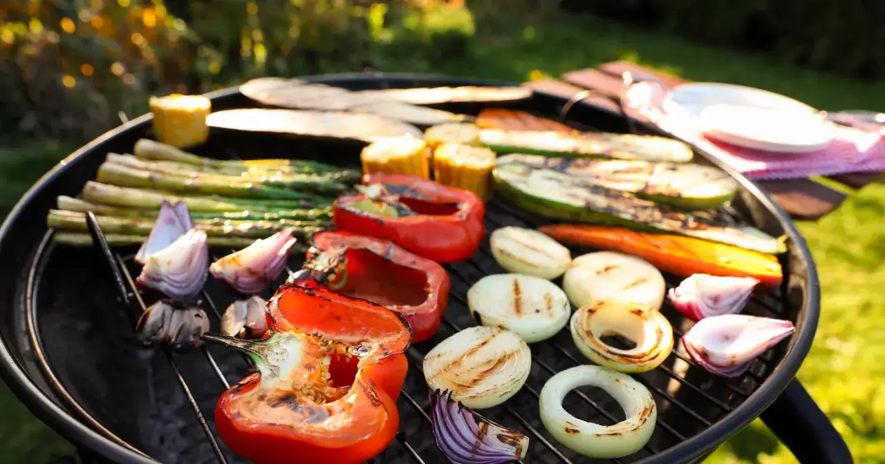 Kolorowe warzywa: papryka, cebula, szparagi, cukinia i kukurydza pieką się na grillu, tworząc idealne danie na letnie popołudnie.