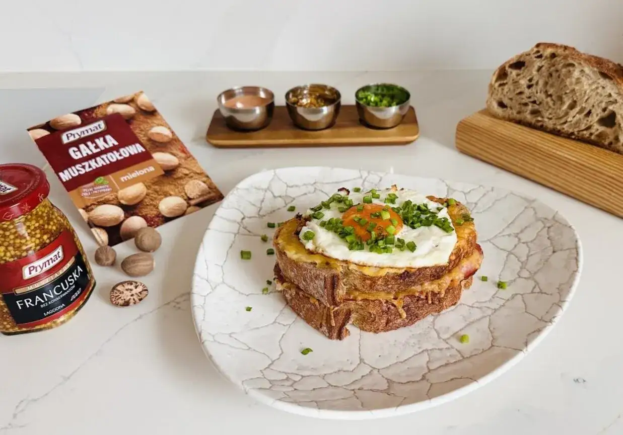 Pyszny croque madame z jajkiem sadzonym i szczypiorkiem, obok musztarda francuska i gałka muszkatołowa.