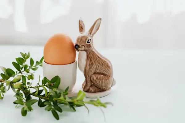 Wielkanocne jajka w kieliszku, obok ceramiczny zajączek i gałązka bukszpanu.