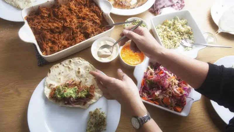 Stół z potrawami do burrito: szarpana wieprzowina, surówka, guacamole i sosy.